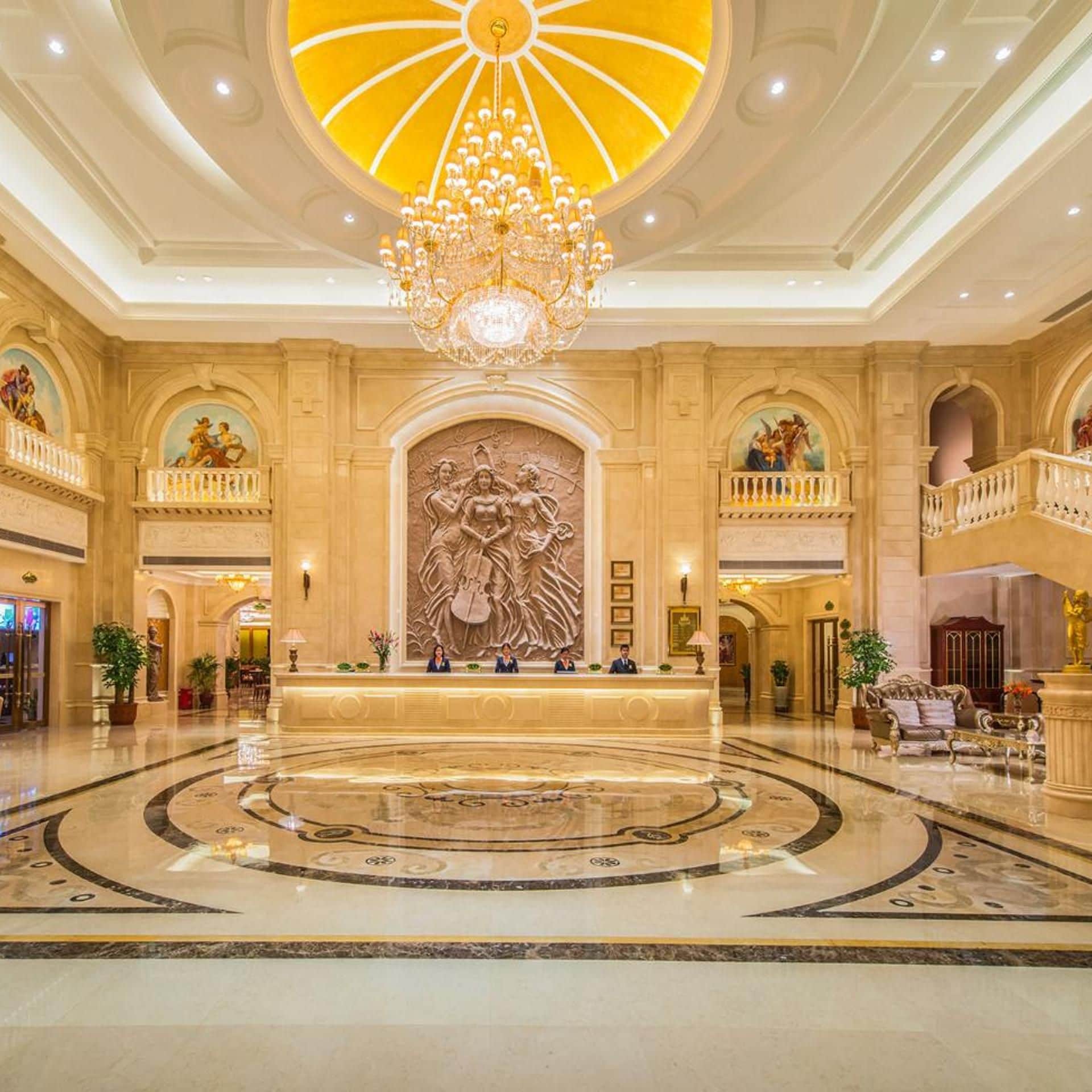 A grand lobby with a central reception desk, a large chandelier, and a marble floor.
