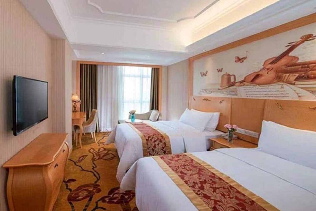 A hotel room with two beds, a TV, a desk, and a mural on the wall.