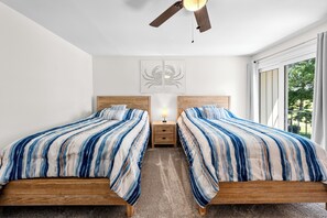 A bedroom with two beds, a ceiling fan, a nightstand with a lamp, and a window with curtains.