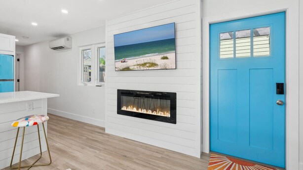 A modern living room with a fireplace, a blue door, and a beach-themed TV on the wall.