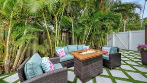 An outdoor patio with wicker furniture, a fire pit, and lush tropical plants.