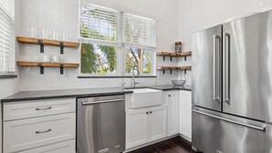 A modern kitchen with white cabinetry, stainless steel appliances, and a window with blinds.