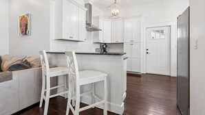 A modern kitchen with white cabinetry, a central island with bar stools, a stainless steel refrigerator, and a pendant light.
