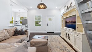 A modern living room with a sofa, ottoman, TV, and decorative items.