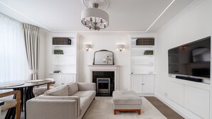 A modern living room with a sofa, ottoman, fireplace, TV, and shelves with decorative items.