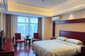 Ein Hotelzimmer mit Bett, Schreibtisch, zwei Stühlen, Fernseher und einem Fenster mit Vorhängen.