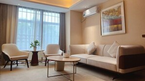 A modern hotel room with a sofa, two armchairs, a round coffee table, a potted plant, and a large window with curtains. - GreenTree Inn (Beijing Olympic Park National Tennis Center Hotel) (Beijing)