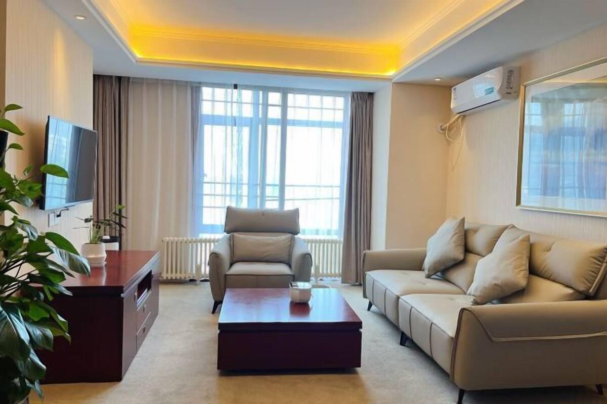 A modern living room with a sofa, a coffee table, a TV, and a large window.