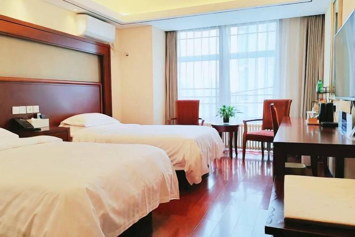 A hotel room with two beds, a desk, a chair, a small table, and a large window.
