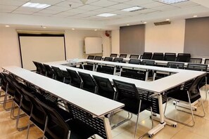 Une salle de conférence avec une longue table, des chaises noires et un tableau blanc.