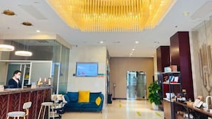 A hotel lobby with a reception desk, a blue sofa with yellow cushions, a large chandelier, and a potted plant. - GreenTree Inn (Beijing Olympic Park National Tennis Center Hotel) (Beijing)
