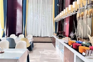 Un espace repas avec des tables et des chaises, un comptoir où sont exposés divers articles, et une fenêtre avec des rideaux.