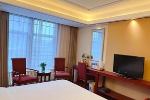 A hotel room with a large bed, two red chairs, a small table with a plant, a television on a wooden stand, and a window with curtains. - GreenTree Inn (Beijing Olympic Park National Tennis Center Hotel) (Beijing)