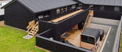 A modern, multi-level residential building with a flat roof, wooden deck, and a small outdoor kitchen area.
