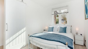 Une chambre à coucher avec un lit, des tables de chevet, une fenêtre et une porte.