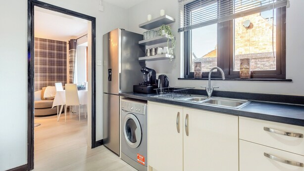 Une cuisine moderne équipée d’un lave-linge intégré, d’une machine à café et d’une fenêtre avec des stores.