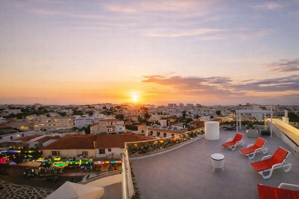 A rooftop terrace with red lounge chairs and a cityscape view at sunset. - Ocean Drive by Check-in Portugal (Albufeira)