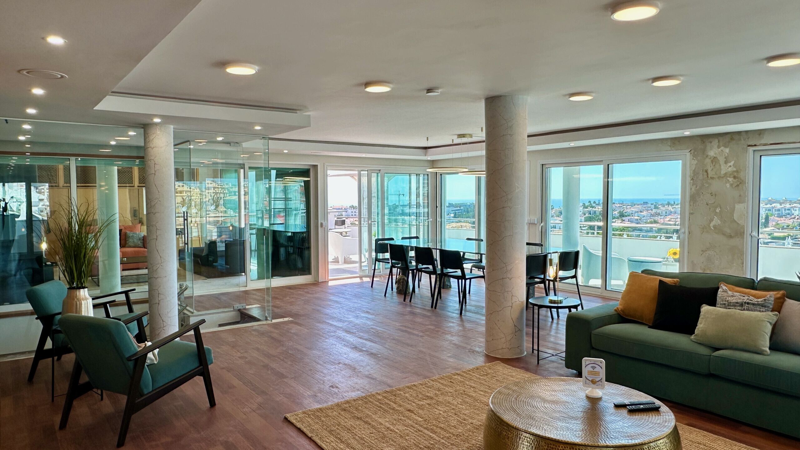 A spacious living area with a green sofa, a round coffee table, and a view of the city through large windows.