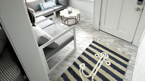 Un intérieur lumineux et blanc, avec un coin salon, une petite table et une porte sur laquelle est apposée une pancarte « Interdiction de fumer ».