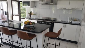 A modern kitchen with a central island, bar stools, a stove, and white cabinetry.