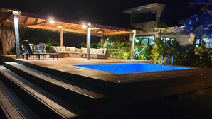 A poolside area with a wooden deck, outdoor seating, and a covered patio.