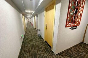 Un pasillo de hotel con piso alfombrado, puertas y un ventanal decorativo.