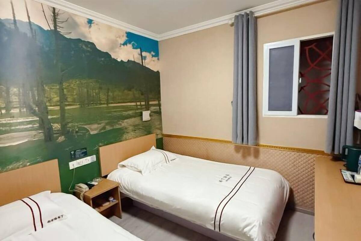 Habitació d'hotel amb dos llits, un mural a la paret, una finestra amb cortines i un escriptori petit amb un telèfon.