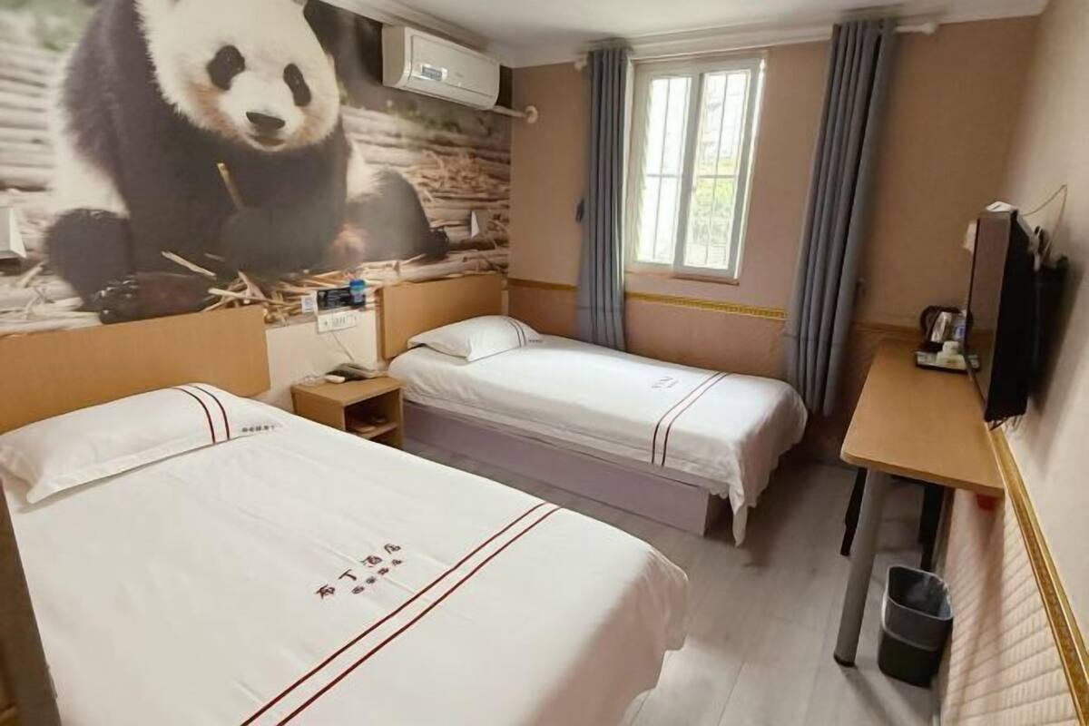Habitació d'hotel amb dos llits, un escriptori, una televisió i un mural de panda a la paret.