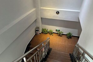 Una escalera con barandillas de metal, piso alfombrado y plantas en el rellano.