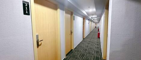 Un couloir d’hôtel avec des portes numérotées 311, 312 et 313, un revêtement de sol en moquette et un extincteur sur le côté droit.