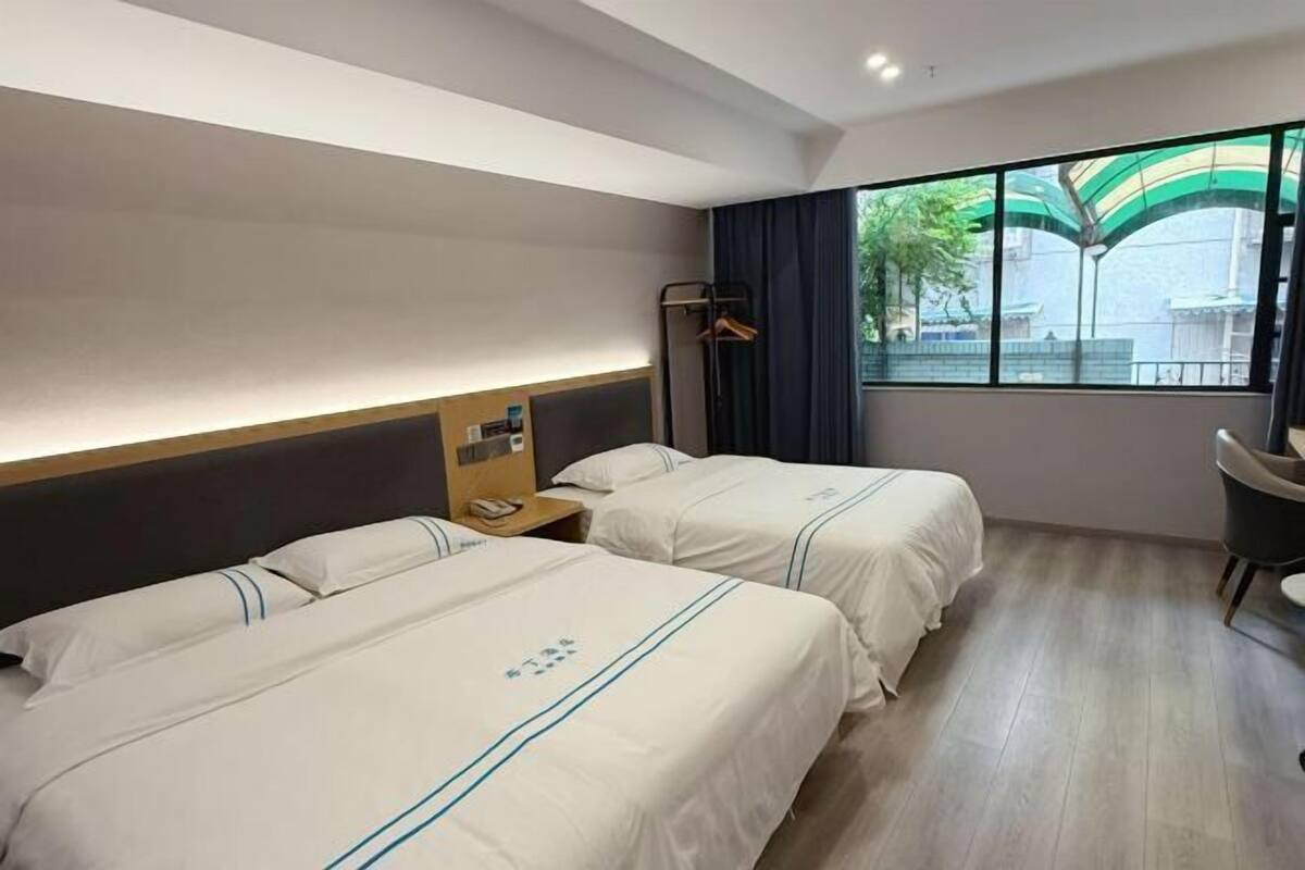 Habitació d'hotel amb dos llits, una escriptori, una cadira, una finestra amb vista a edificis i una mànega.