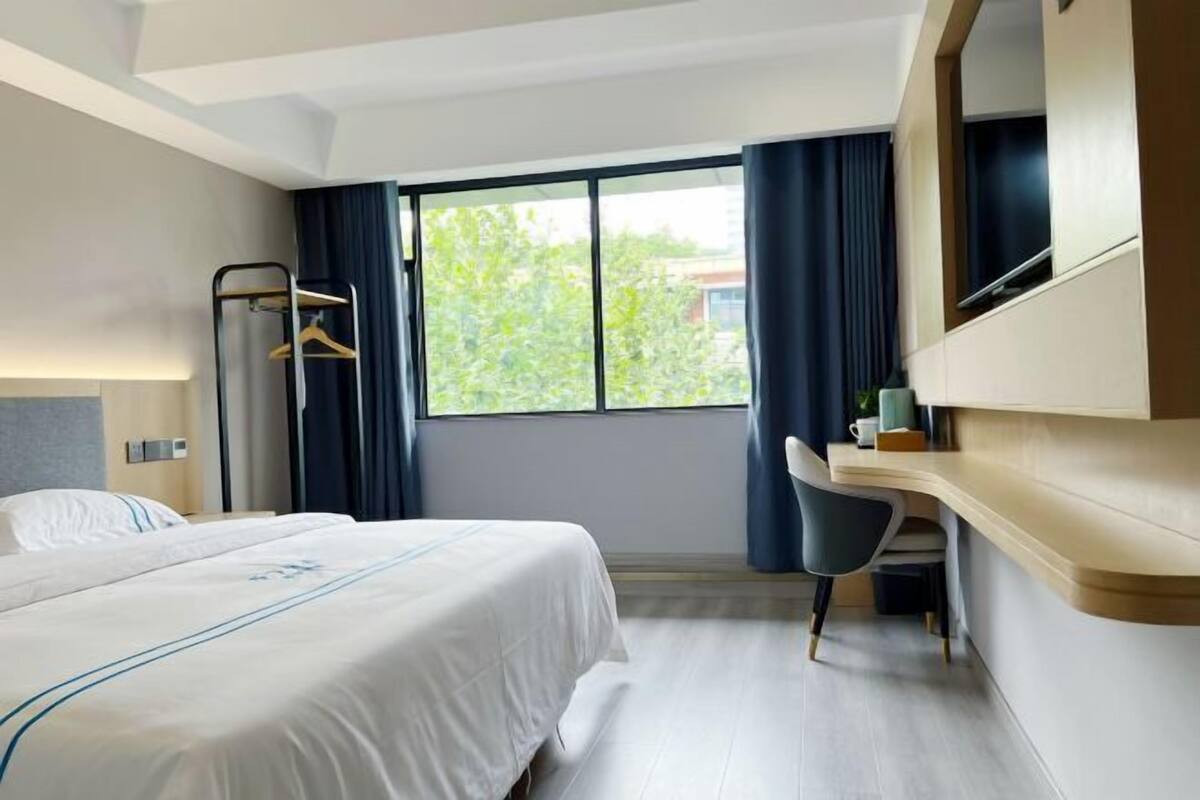 Habitació d'hotel amb llit, escriptori, cadira, televisió i finestra amb cortines.