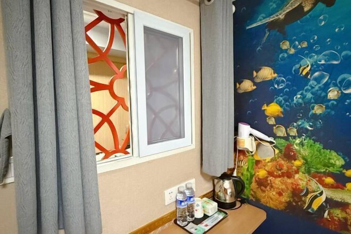 Una habitació amb finestra, cortina, mural de peixos, cafetera i safata amb ampolles i una caixa de mocadors.