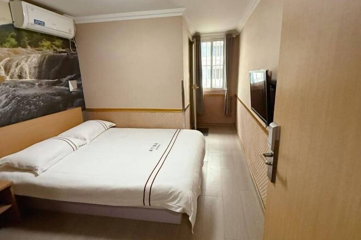 Habitació d'hotel amb un llit, una televisió, una finestra i un aire condicionat de paret.