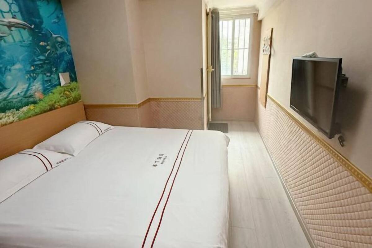 Habitació d'hotel amb un llit, televisió, un mural i una finestra.