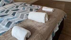 Una cama bien hecha con una colcha estampada y dos toallas dobladas, un armario con espejo y suelo de madera.