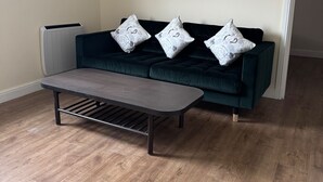 Una sala de estar moderna con un sofá verde oscuro, tres almohadones estampados y una mesa de centro de madera oscura.