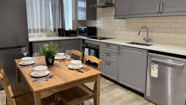 Una cocina moderna con gabinetes grises, electrodomésticos de acero inoxidable y una mesa de comedor de madera dispuesta para cuatro.