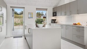A modern kitchen with a large island, built-in appliances, and a view of the outdoors. - 5 Star Holiday Home in Lokken (Lokken)