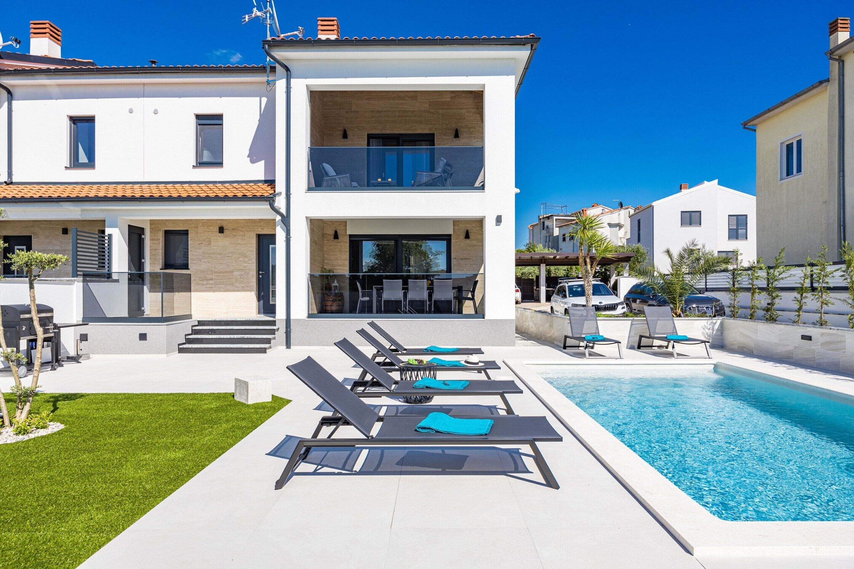 Une maison moderne à deux étages, dotée d’une piscine, de chaises longues et d’une pelouse bien entretenue.
