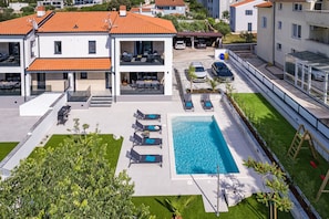 Ett modernt hus i två våningar med en swimmingpool, en uteplats och ett garage.
