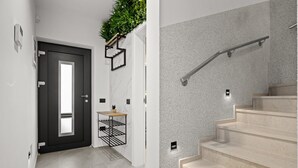 Un intérieur moderne avec une porte sombre, une petite table ornée d’une plante et un escalier muni d’une main courante.