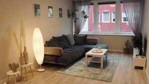 A modern living room with a dark grey sofa, a white coffee table, and a large floor lamp. There are framed pictures on the wall and a window with sheer curtains. - Apartment in the heart of Braunschweig (Braunschweig)