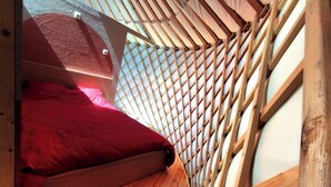 A small, sloped-roofed room with a wooden floor and a single bed with a red blanket. - Camellia is a beautiful yurt 10 minutes walk from Pairi Daiza (Brugelette)