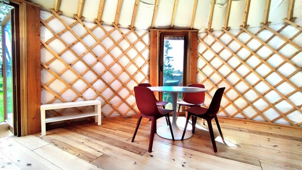 A room with a wooden floor, a round table with chairs, a bench, and a lattice wall. - Camellia is a beautiful yurt 10 minutes walk from Pairi Daiza (Brugelette)