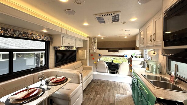 A well-lit RV interior with a dining area, kitchenette, and seating. - Hillside Haven in Berryessa (San Jose)