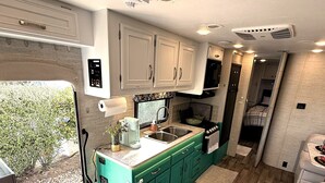 A compact RV kitchen with teal cabinetry, a sink, and a stove. - Hillside Haven in Berryessa (San Jose)