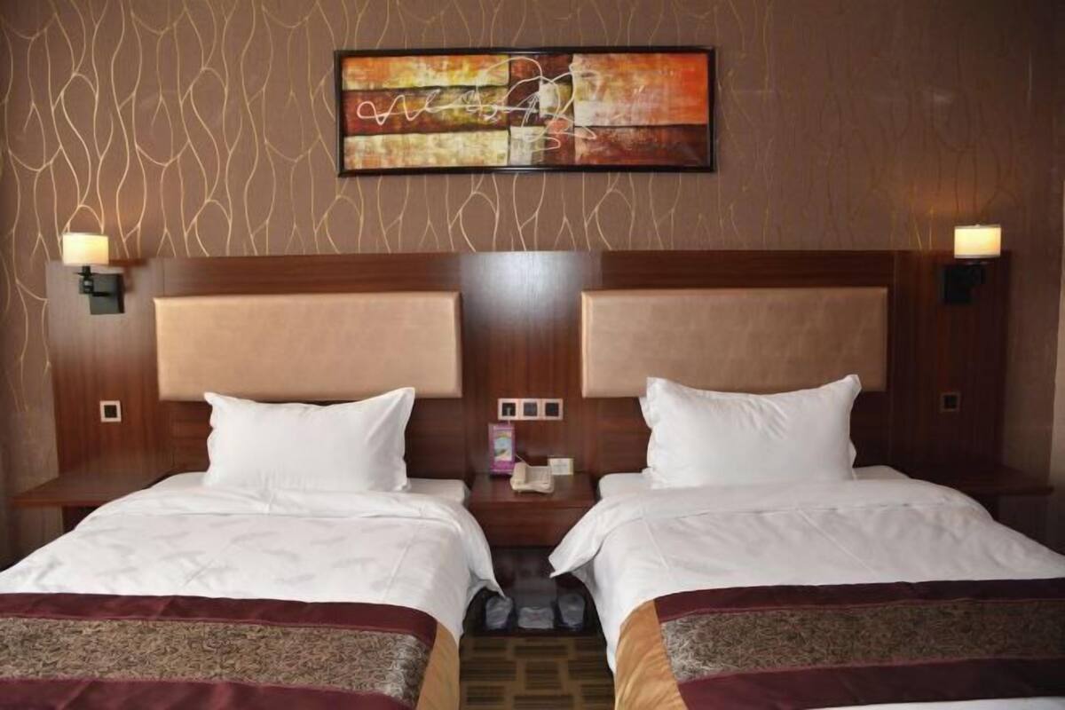 Een hotelkamer met twee bedden, een groot kunstwerk erboven en een kamerwand met patroon.