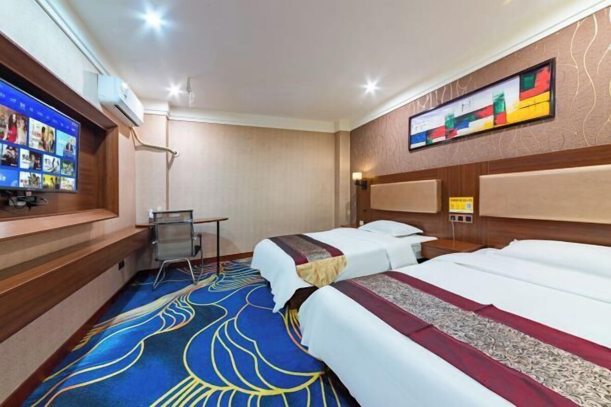 Una habitación de hotel con una cama grande, un escritorio, un televisor y una alfombra estampada.