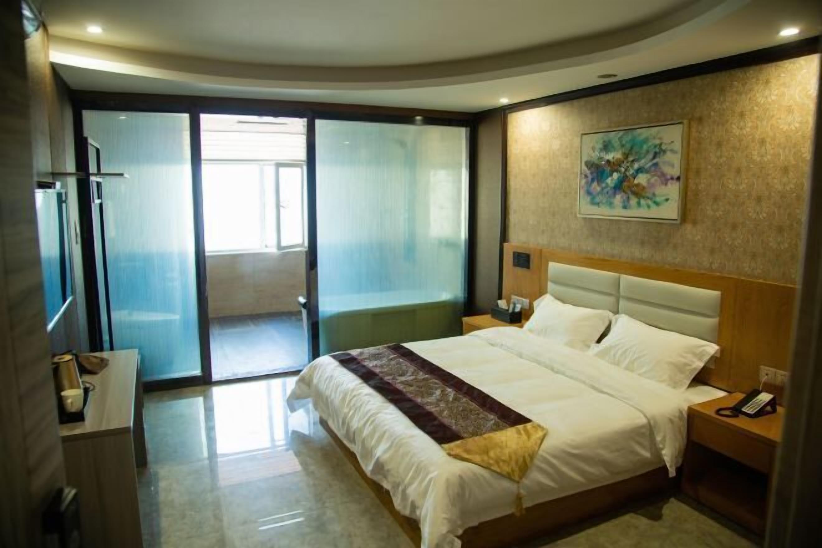 Habitación de hotel con una cama grande, una mesita de noche, un teléfono en la pared y una puerta corrediza de vidrio que da a un balcón.